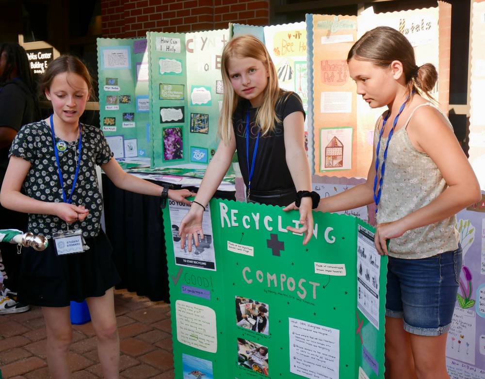 Three students hold up a recycling and compost sign